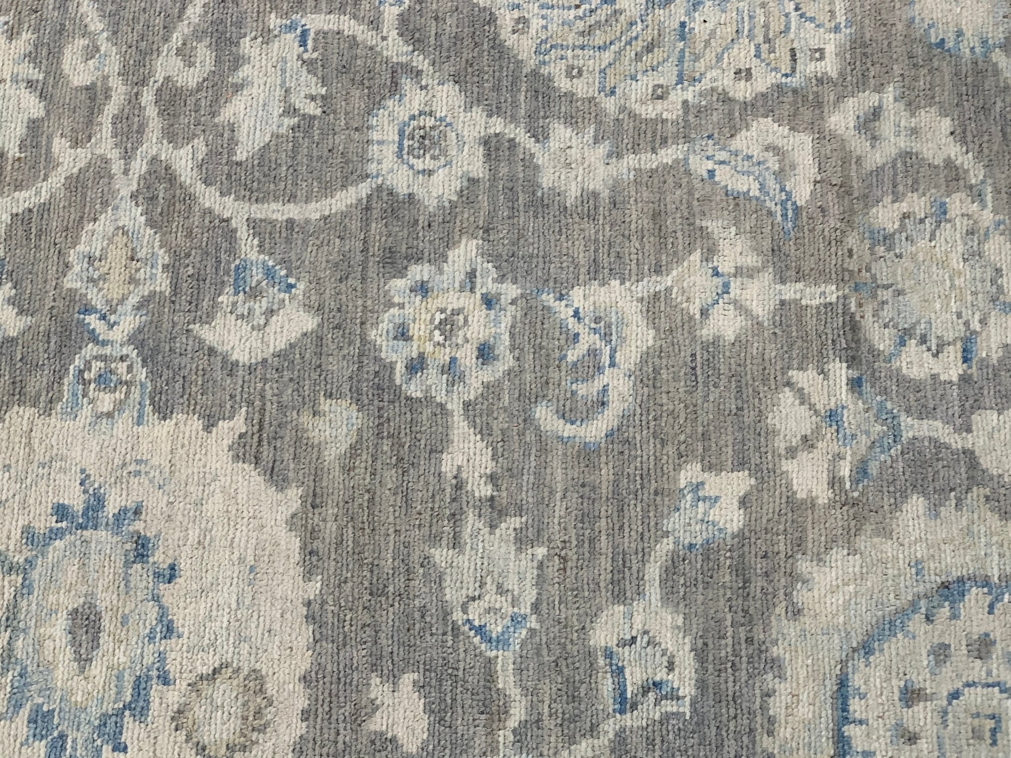 A handmade Afghan Chobi rug featuring a traditional floral pattern in shades of grey and blue.