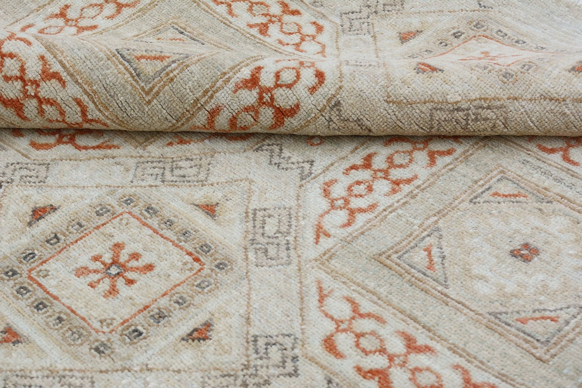 A handmade Afghan Chobi rug featuring a geometric pattern in soft orange and beige tones.