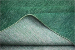 A corner of a handwoven green overdyed Afghan Chobi rug showing its wool pile and cotton backing.