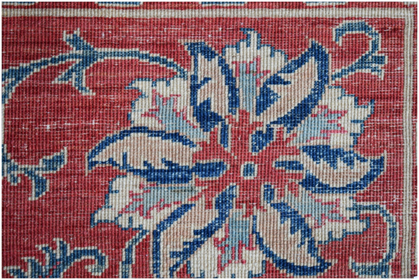 A close-up of a handwoven Afghan Chobi rug featuring a traditional blue and cream floral motif.
