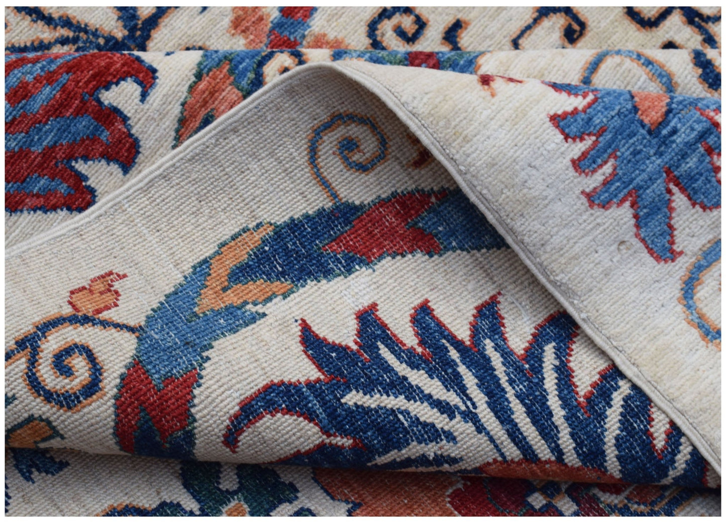 A folded Afghan Chobi rug featuring a traditional floral Suzani pattern in blue, red, and cream.