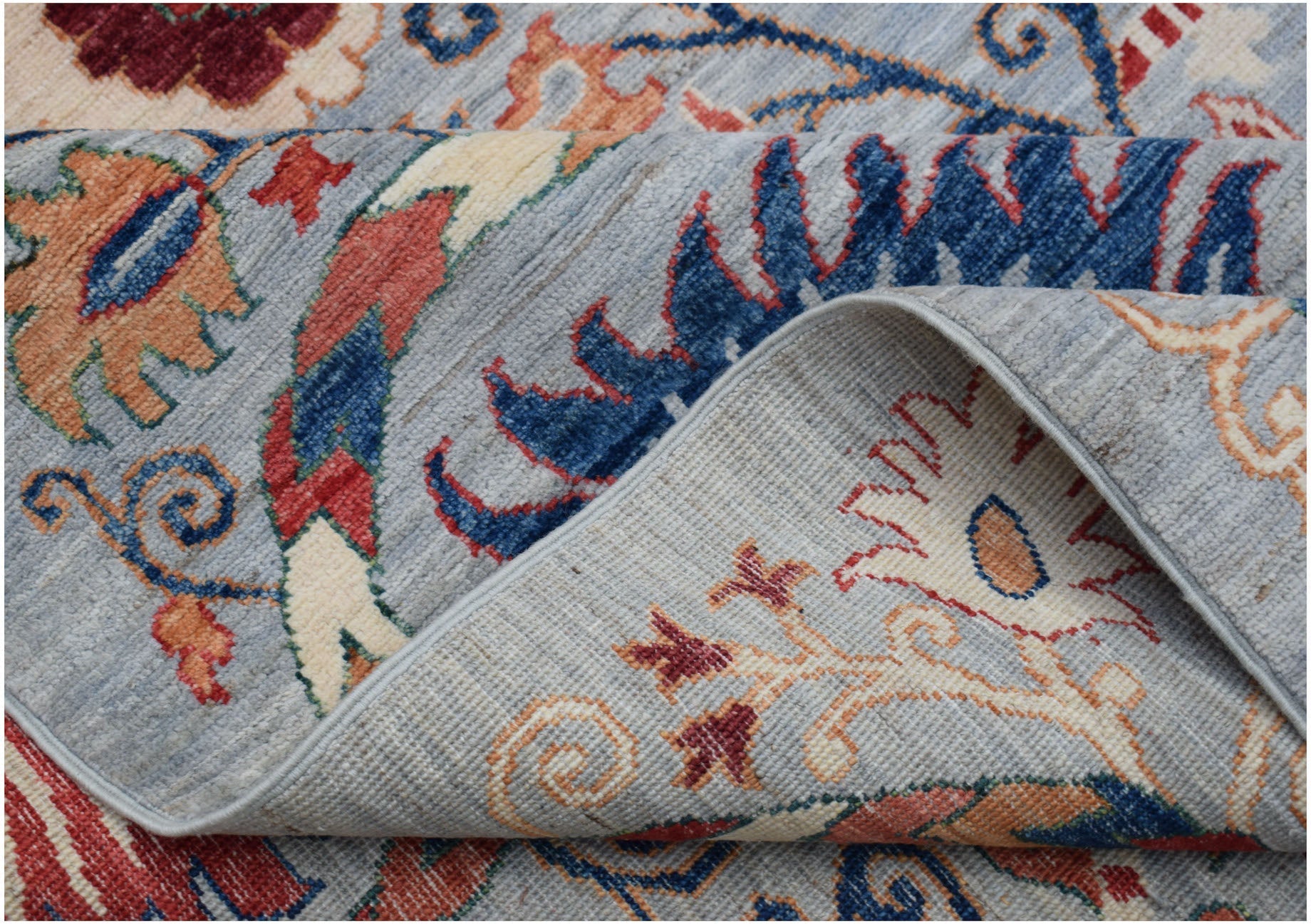 A folded Afghan Chobi rug featuring a traditional Suzani floral pattern in blue, red, and cream.