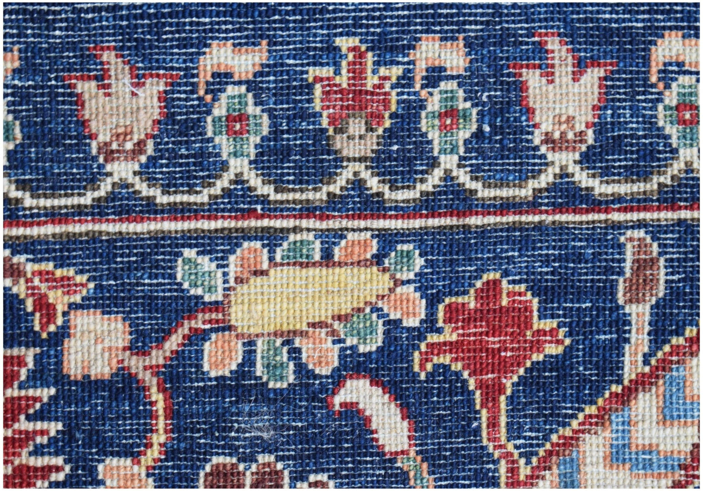 A close-up of a handmade Afghan Chobi rug featuring intricate floral patterns in a deep blue field.