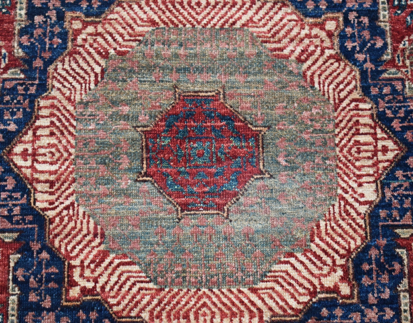 A handwoven Afghan Chobi runner featuring a detailed red and blue Mamluk medallion on a green field.