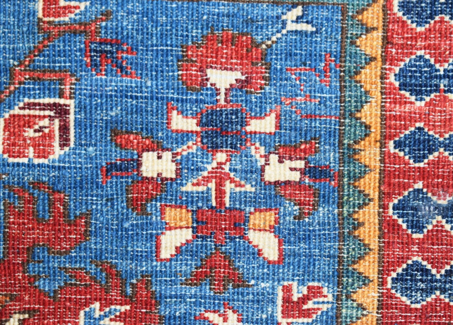A close-up of a hand-knotted Afghan Chobi runner featuring intricate floral motifs in blue and red.