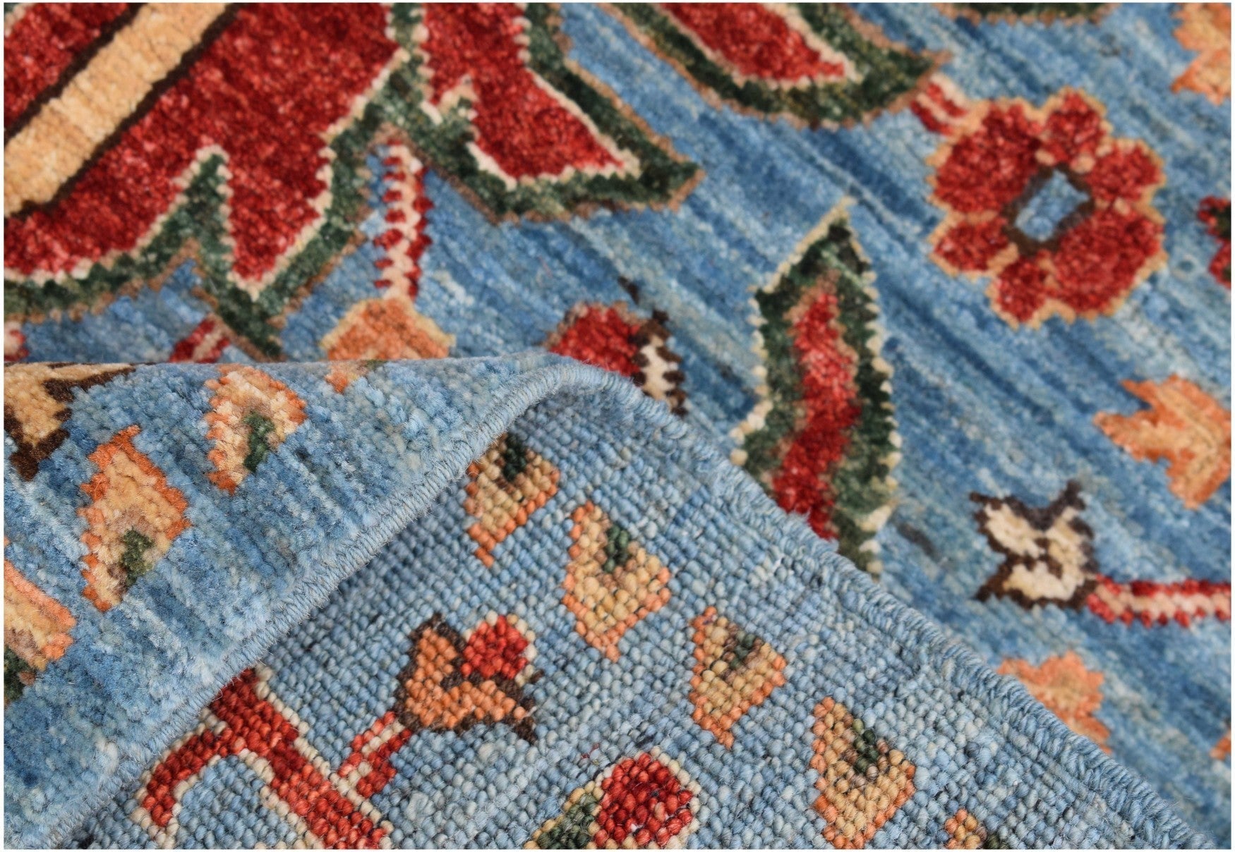 A handmade Afghan Chobi runner featuring a floral pattern in red and blue on a wool pile.