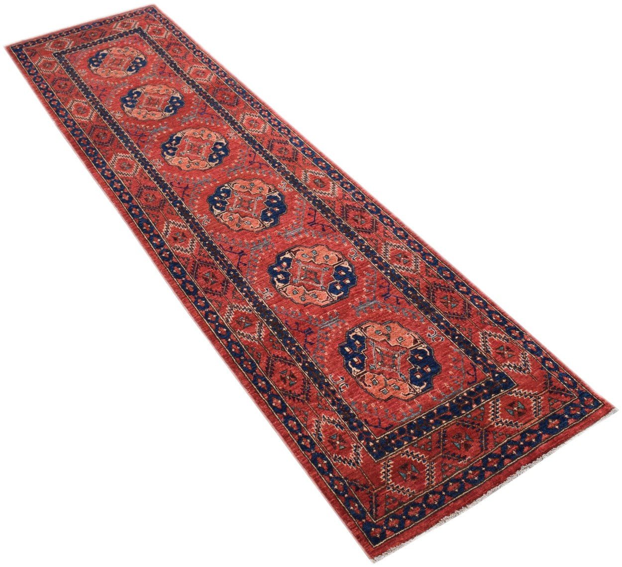 A handmade Afghan Chobi runner rug featuring a red field with repeating blue and peach medallions.