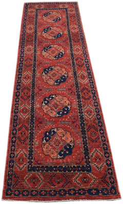A handmade Afghan Chobi runner rug featuring a red field with repeating blue and tan medallions.