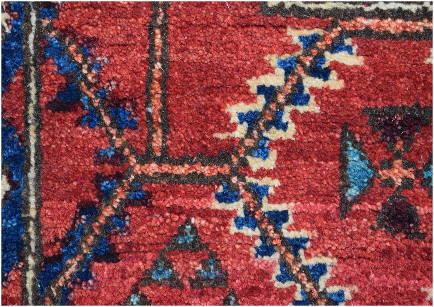 A close-up of an Afghan Chobi runner featuring intricate geometric patterns in red, blue, and cream.