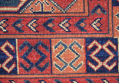 A close-up of a handwoven Afghan Chobi runner featuring geometric patterns in red and blue wool.