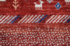 A handmade Afghan Chobi runner featuring a red wool pile with white animal and geometric motifs.