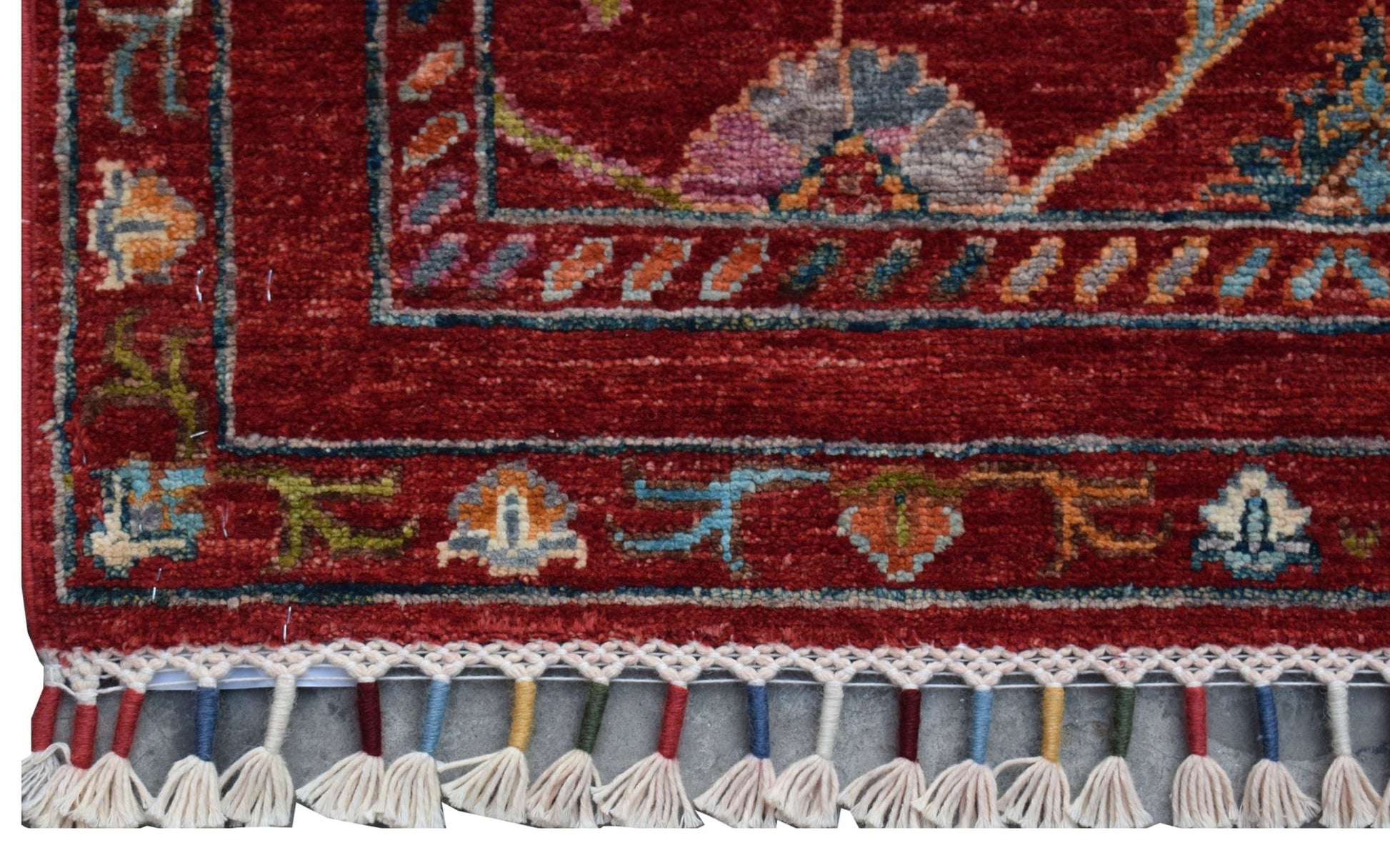 A handmade Afghan Chobi runner featuring a red field with floral motifs and a tasseled fringe.