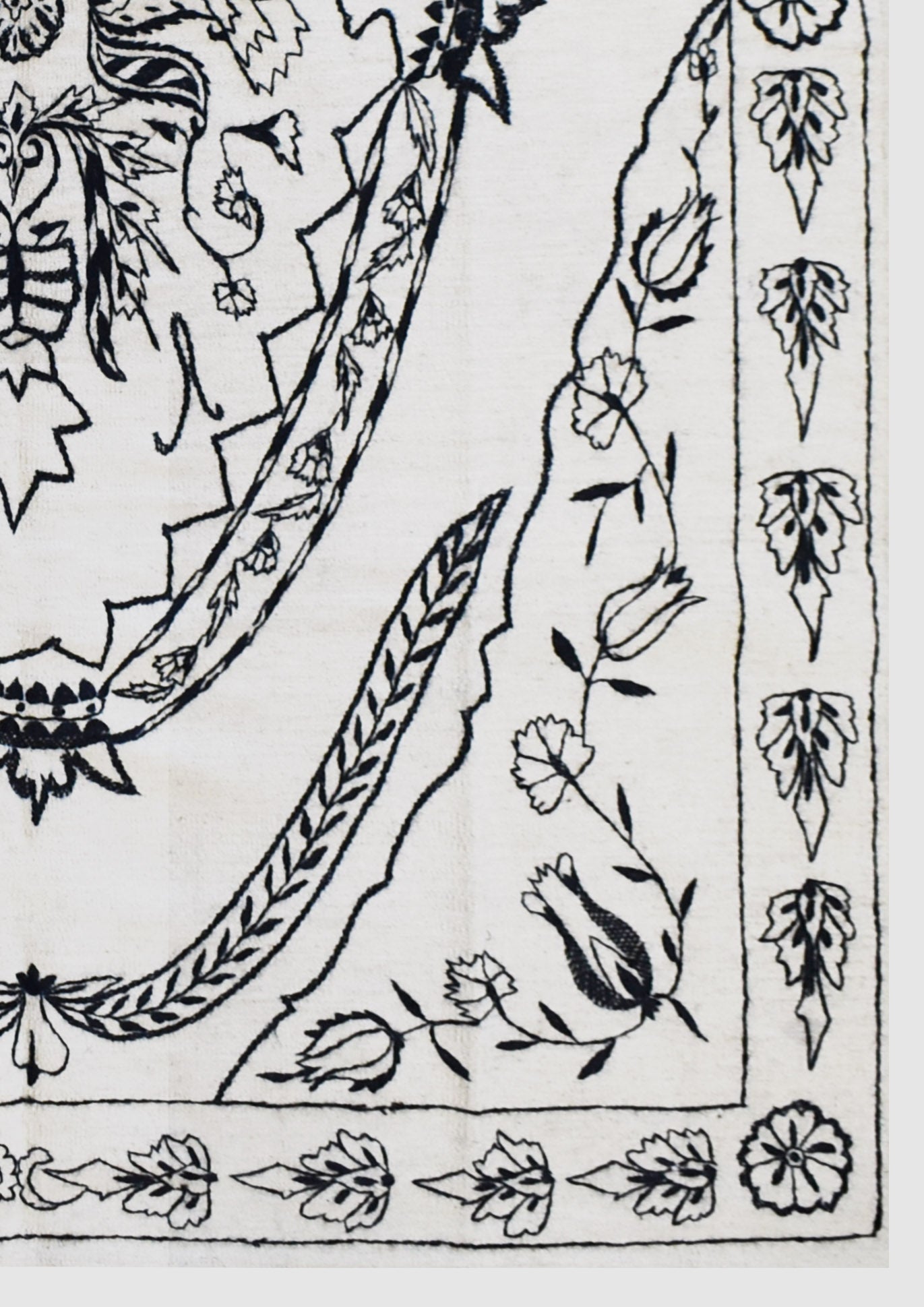 A close-up of a handmade Afghan wool kilim featuring intricate black floral embroidery on white.