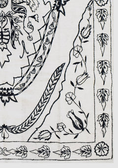 A close-up of a handmade Afghan wool kilim featuring intricate black floral embroidery on white.