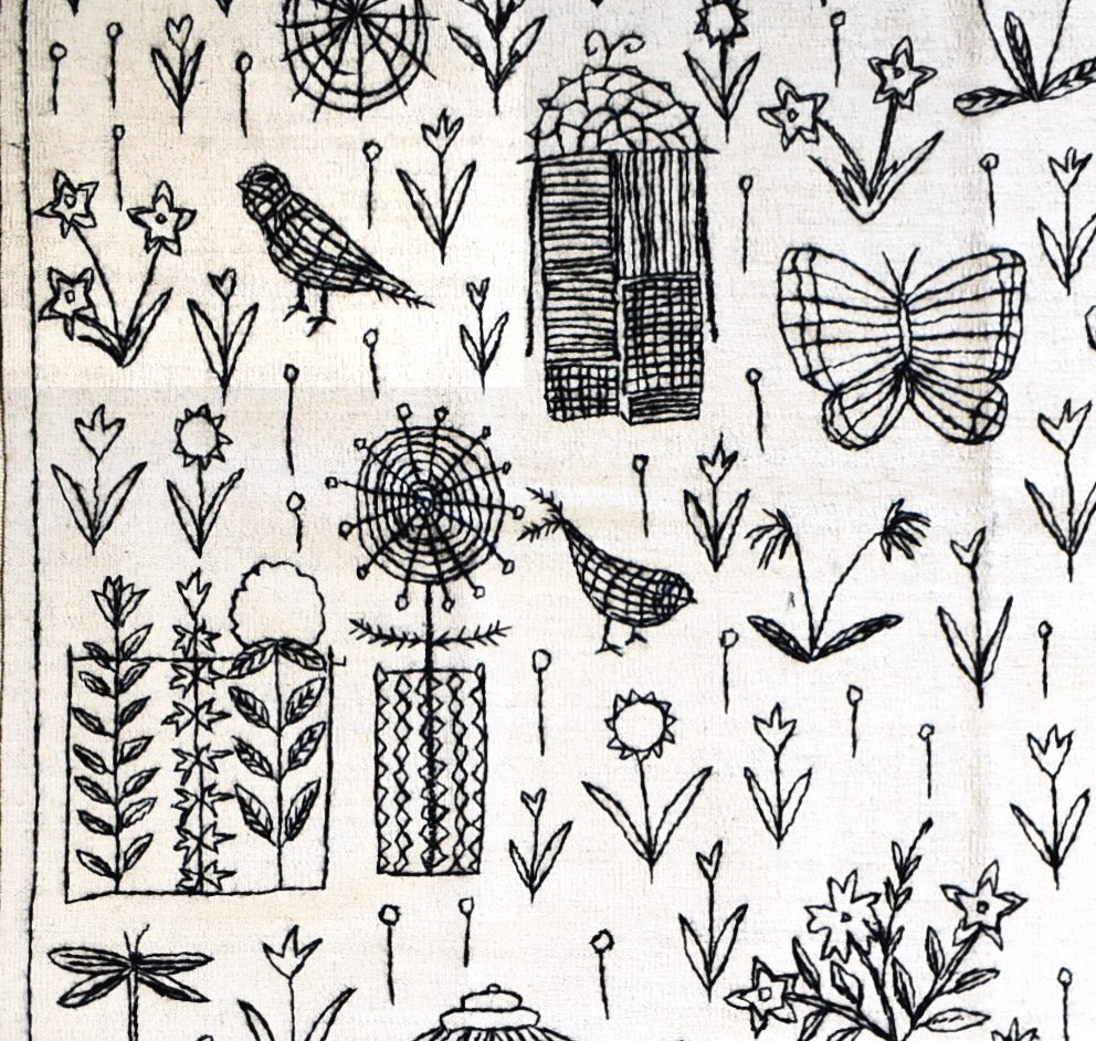 A handmade Afghan kilim featuring black embroidered botanical and animal motifs on a white base.