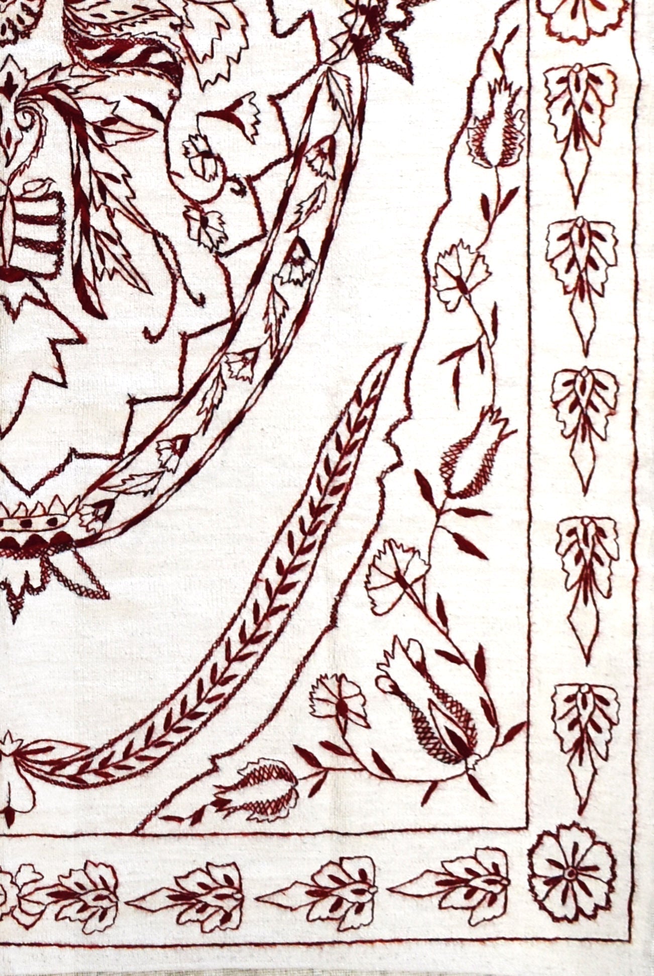 A close-up of an Afghan kilim featuring intricate dark red floral embroidery on a cream background.