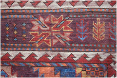 A close-up of a handwoven Afghan rug featuring geometric floral motifs in red, blue, and yellow.