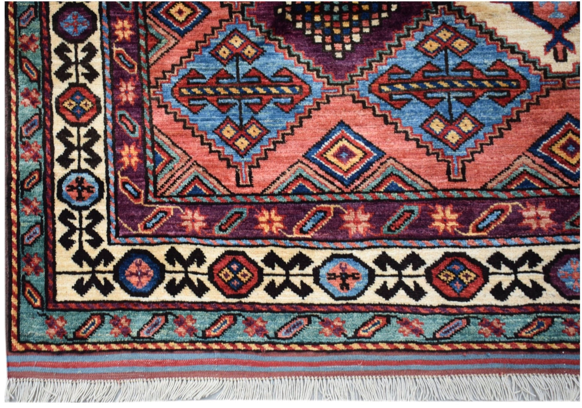 A handwoven Afghan Herati rug featuring geometric diamond patterns in red, blue, and purple wool.