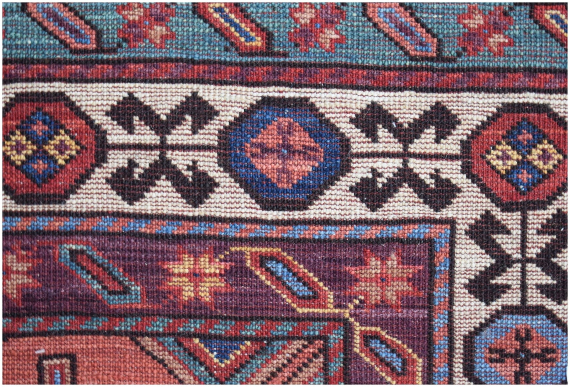 A close-up of an Afghan Herati rug featuring intricate geometric patterns in red, blue, and cream.