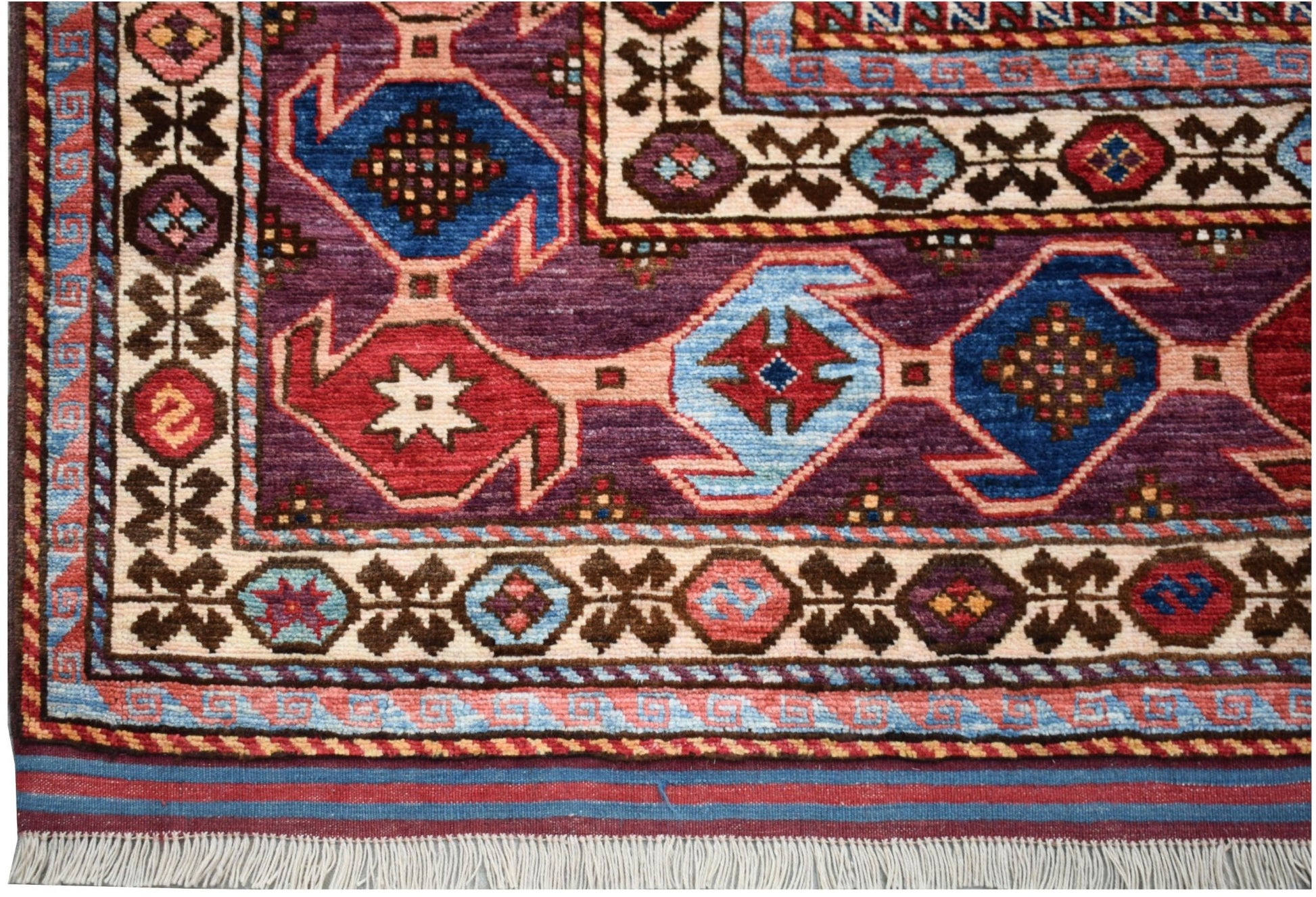 A handmade Afghan Herati rug featuring geometric patterns in purple, red, and blue wool.