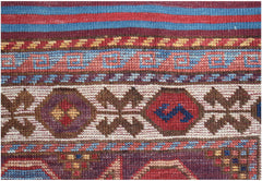 A close-up of a handwoven Afghan Herati rug featuring geometric patterns in red, blue, and brown.