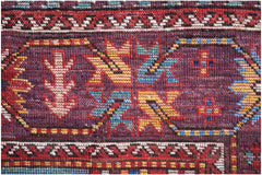 A close-up of an Afghan Herati runner featuring a deep purple field with geometric floral motifs.
