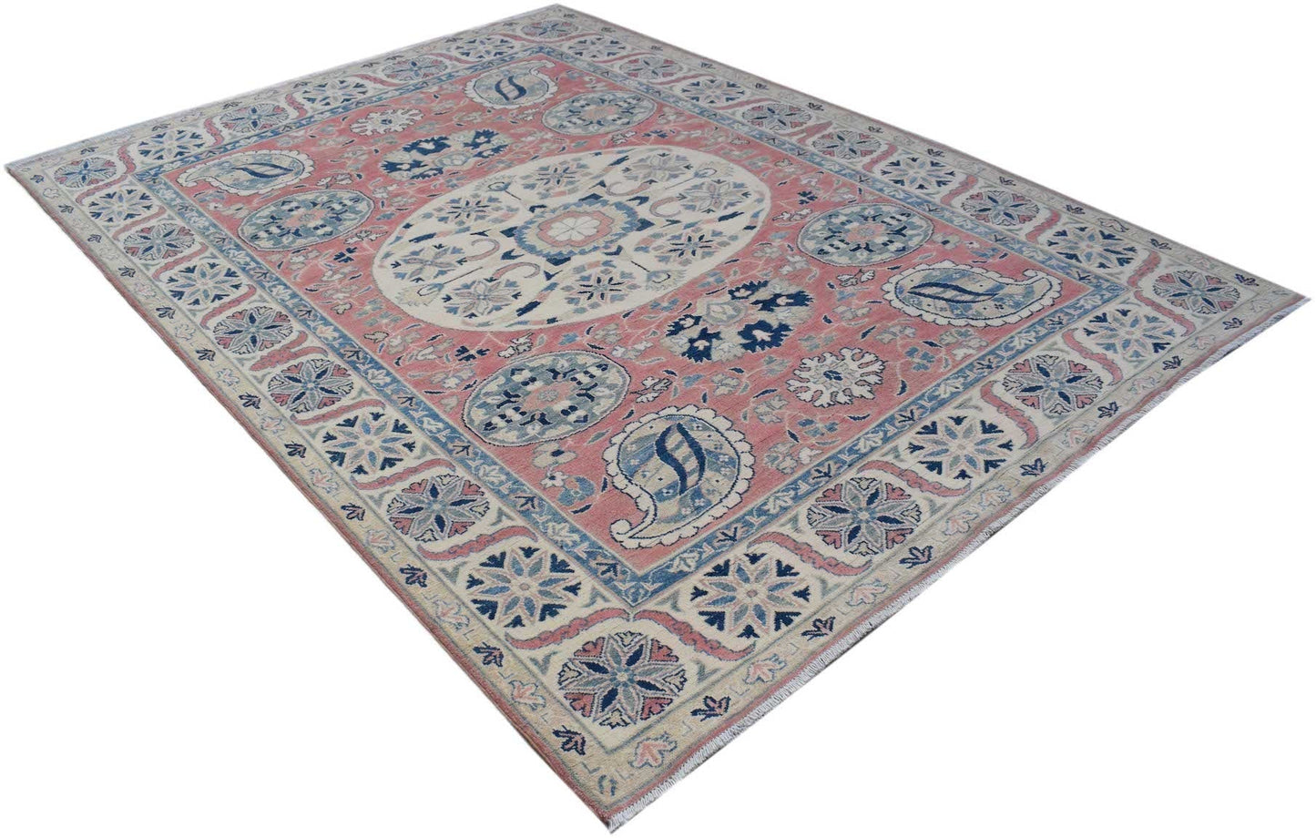 A handmade Afghan Kazakh rug featuring traditional blue and cream floral motifs on a pink field.