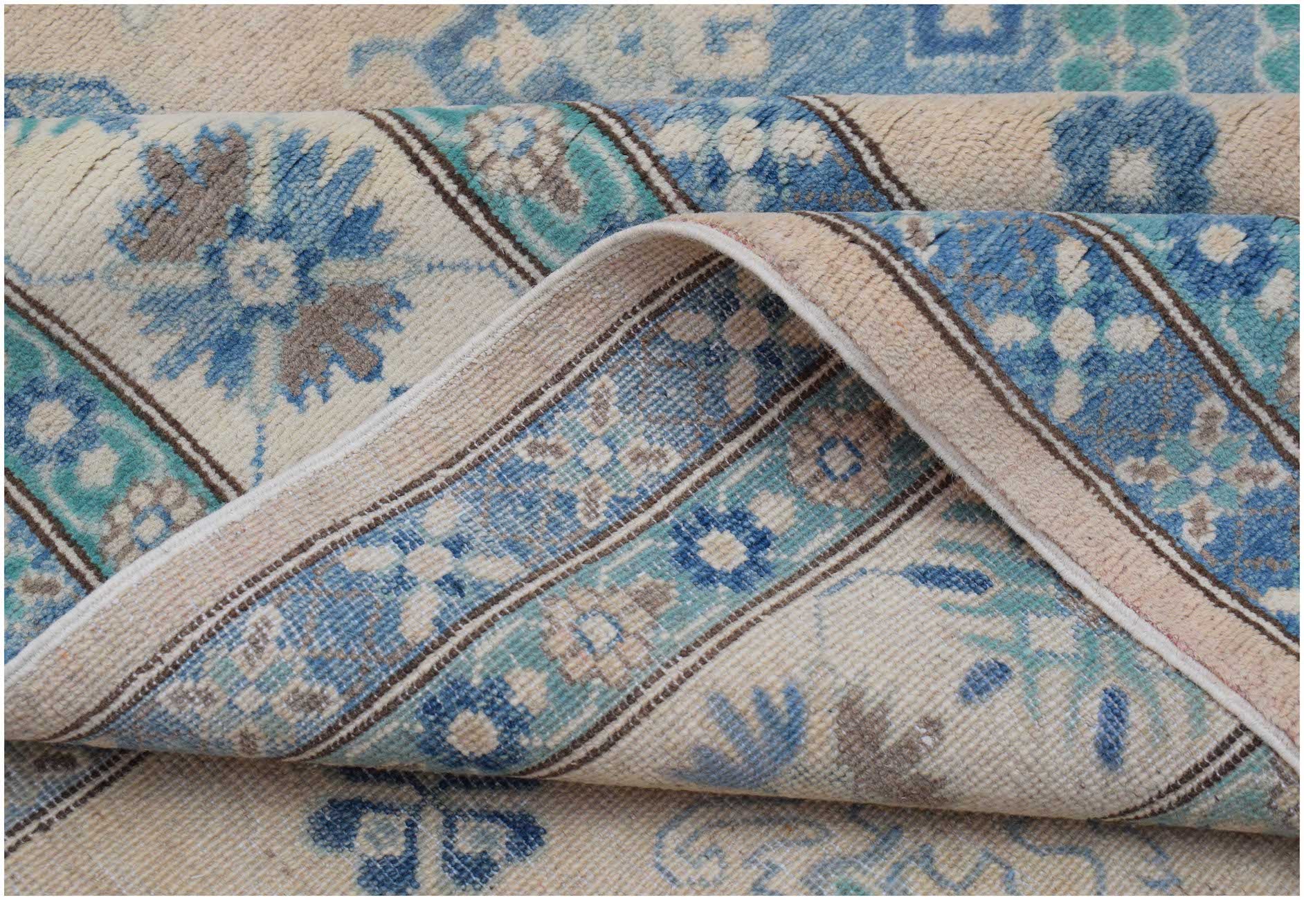 A handmade Afghan Kazakh rug featuring a beige background with blue and grey floral patterns.