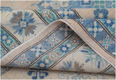 A handmade Afghan Kazakh rug featuring a beige background with blue and grey floral patterns.