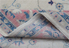 A handmade Afghan Kazakh rug featuring traditional blue and pink floral motifs on a cream base.