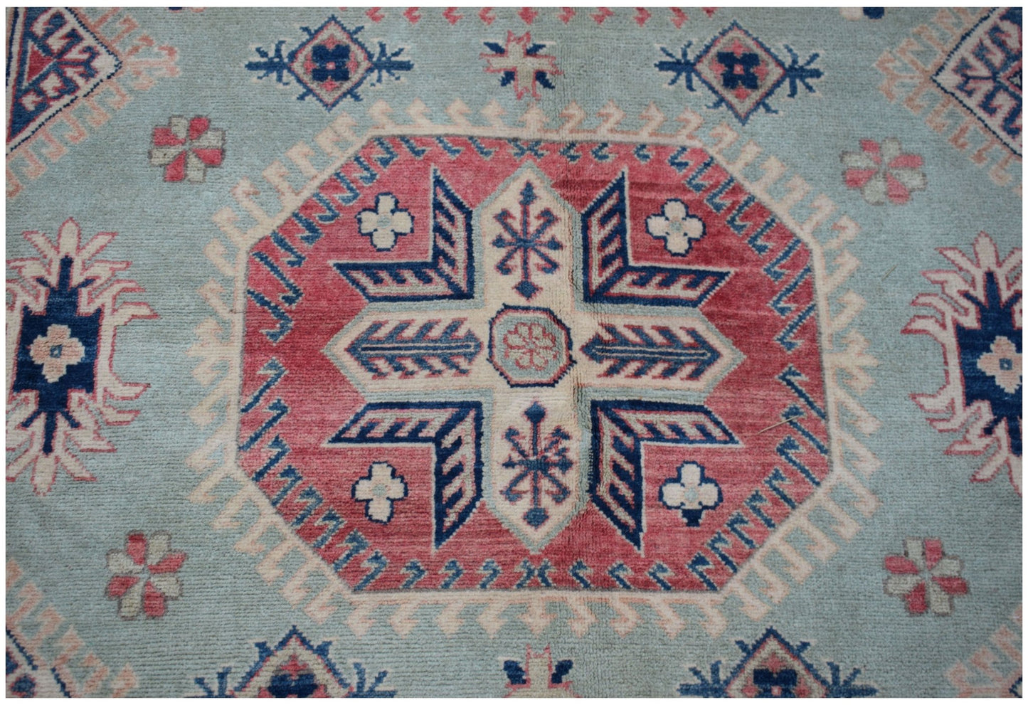A handmade Afghan Kazakh rug featuring a central geometric medallion on a light blue field.
