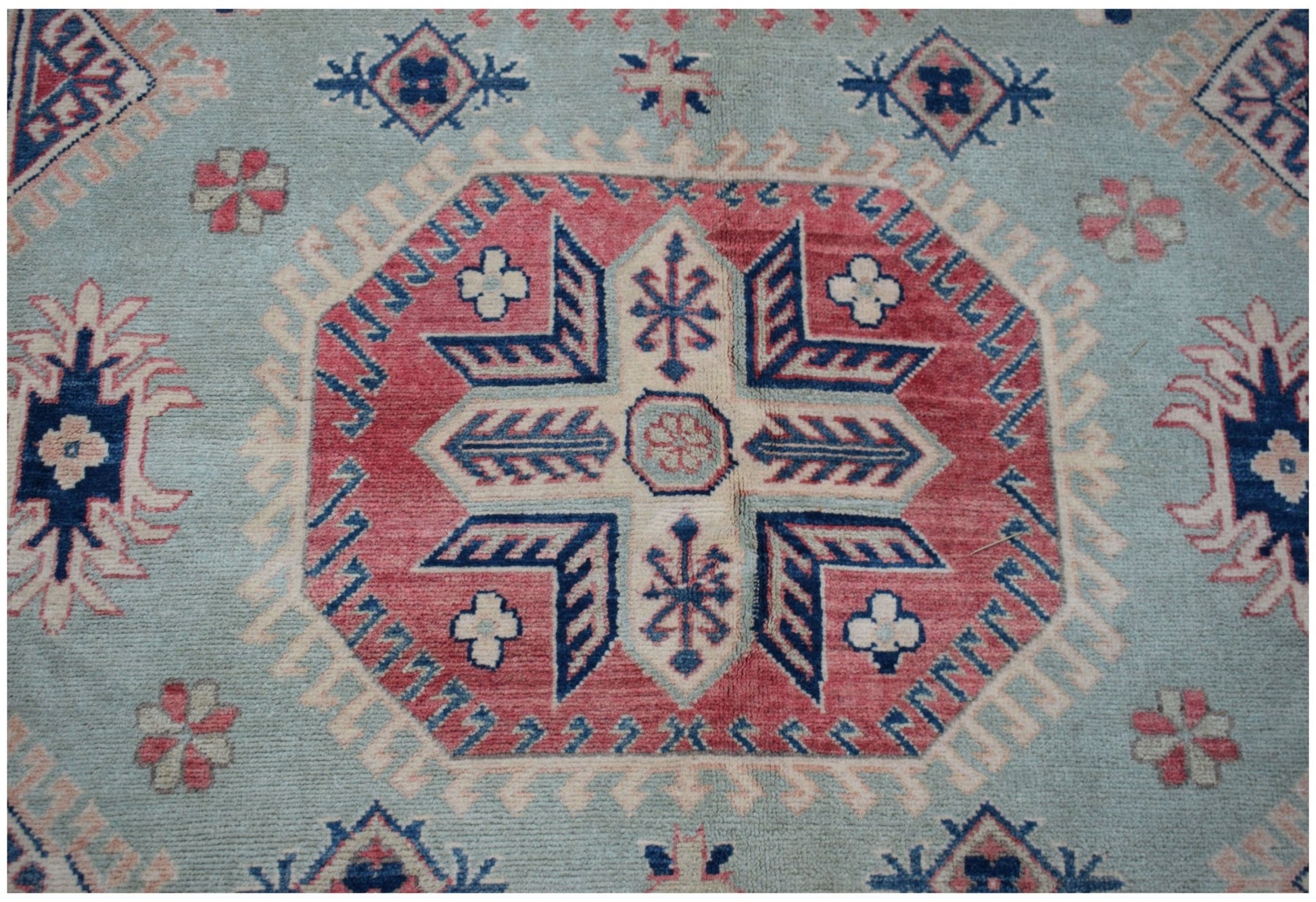 A handmade Afghan Kazakh rug featuring a central geometric medallion on a light blue field.