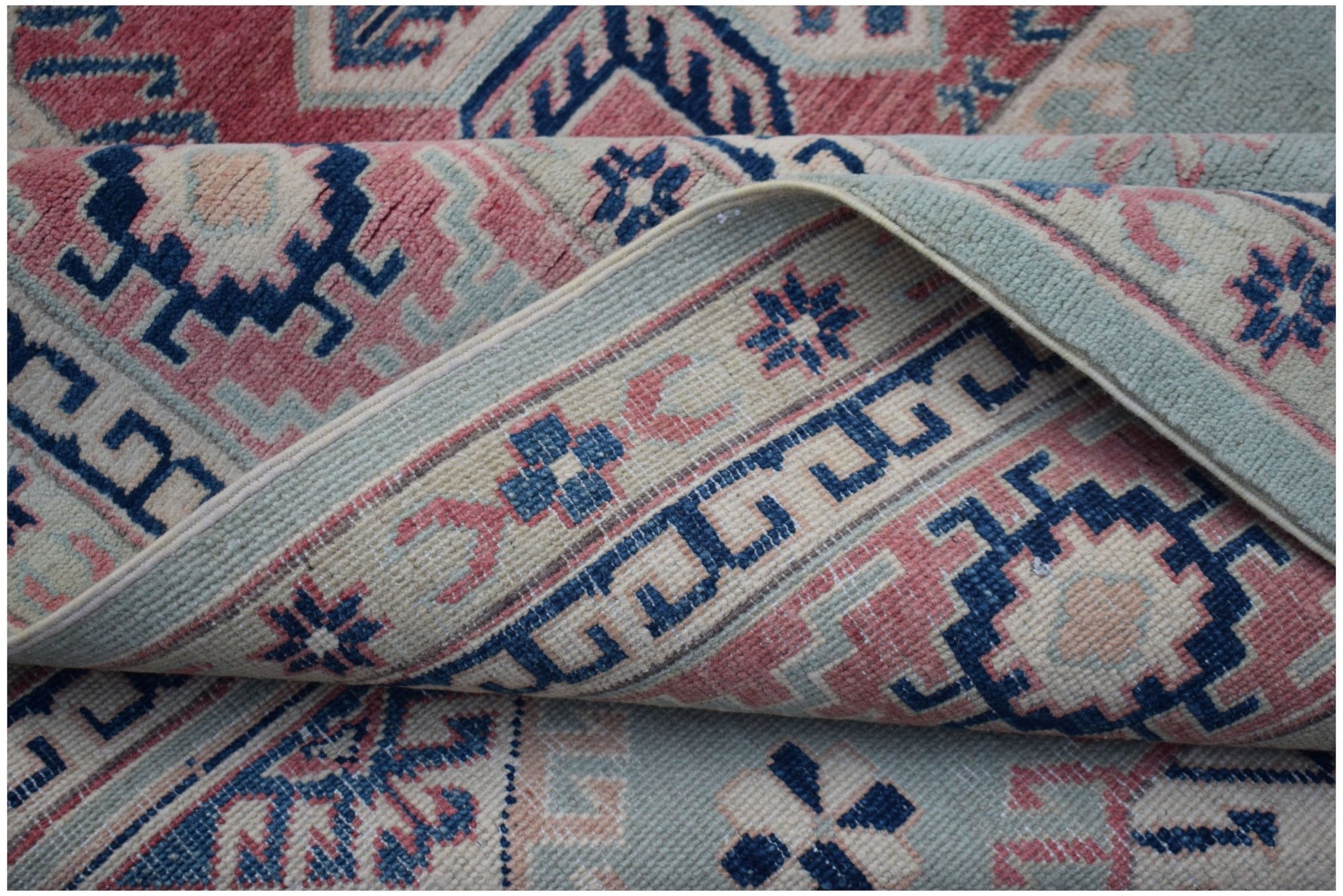 A handmade Afghan Kazakh rug featuring traditional geometric motifs in blue, pink, and cream wool.