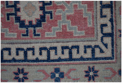 A close-up of an Afghan Kazakh rug featuring traditional geometric patterns in blue, red, and tan.