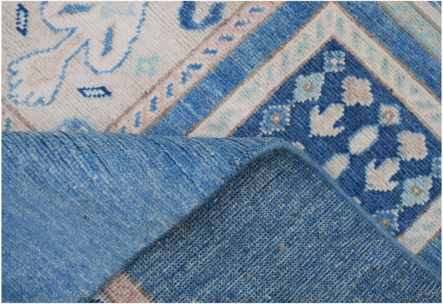 A corner of a handmade Afghan Kazakh rug with blue and beige geometric patterns.