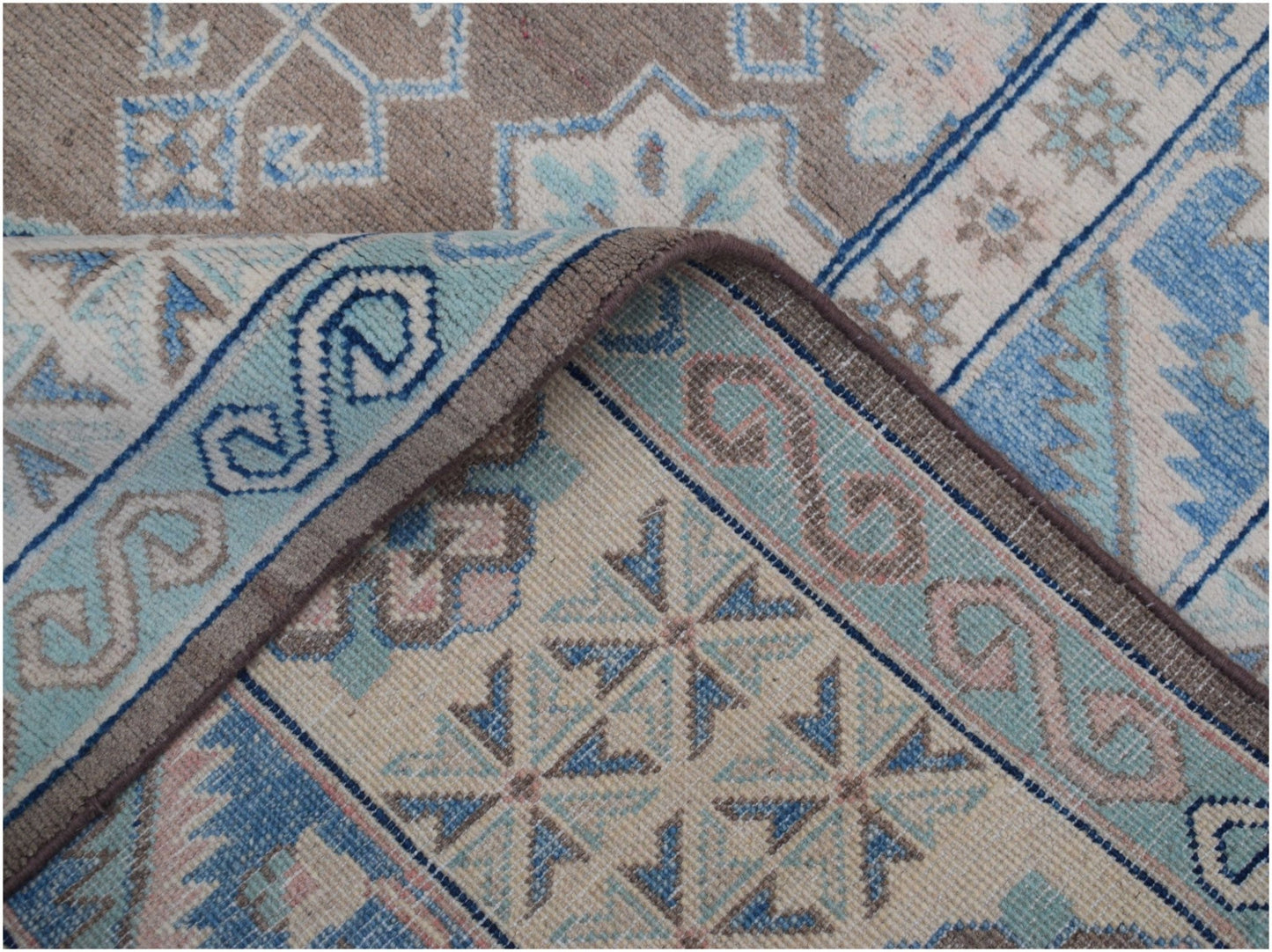 A handmade Afghan Kazakh rug featuring a geometric pattern in shades of beige, blue, and grey.