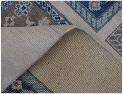 A corner of a handmade Afghan Kazakh wool rug is folded back to reveal its cotton foundation.