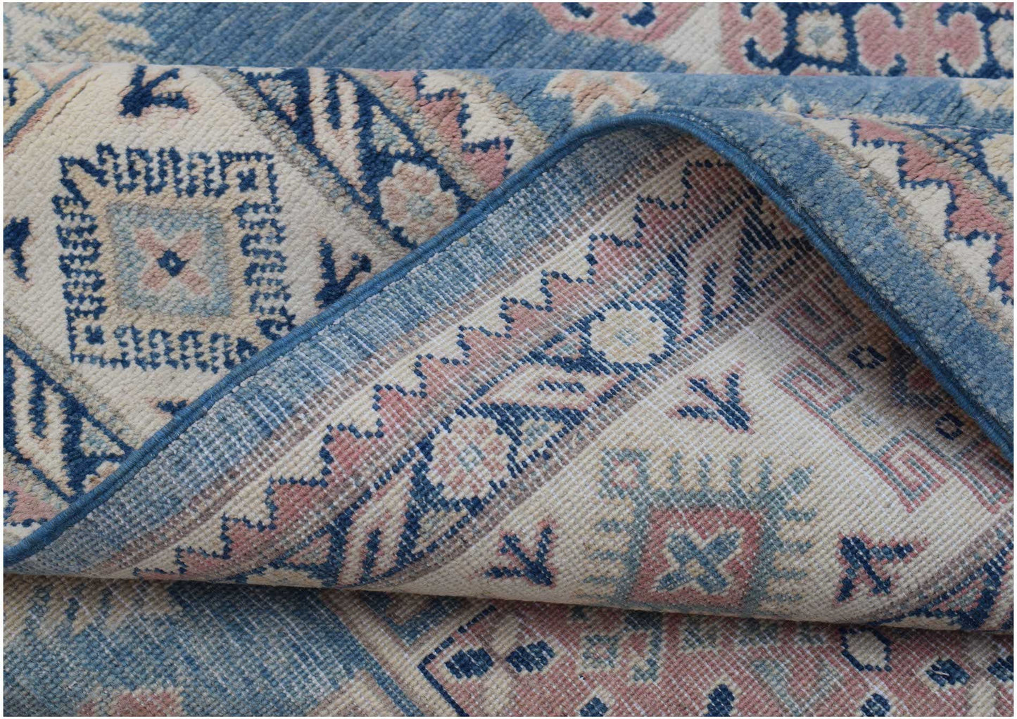 A folded Afghan Kazakh rug featuring traditional geometric motifs in blue, pink, and cream wool.