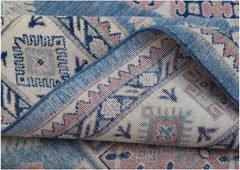 A folded Afghan Kazakh rug featuring traditional geometric motifs in blue, pink, and cream wool.
