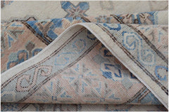 A corner of a handmade Afghan Kazakh wool rug with a traditional pattern in blue and soft pink.