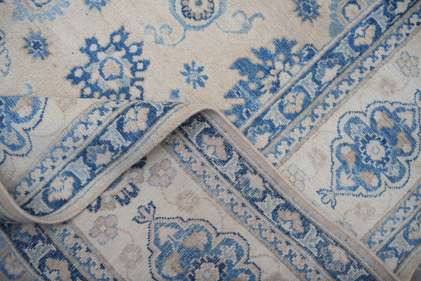 A handmade Afghan Kazakh rug featuring a beige background with intricate blue floral patterns.