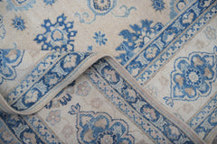 A handmade Afghan Kazakh rug featuring a beige background with intricate blue floral patterns.
