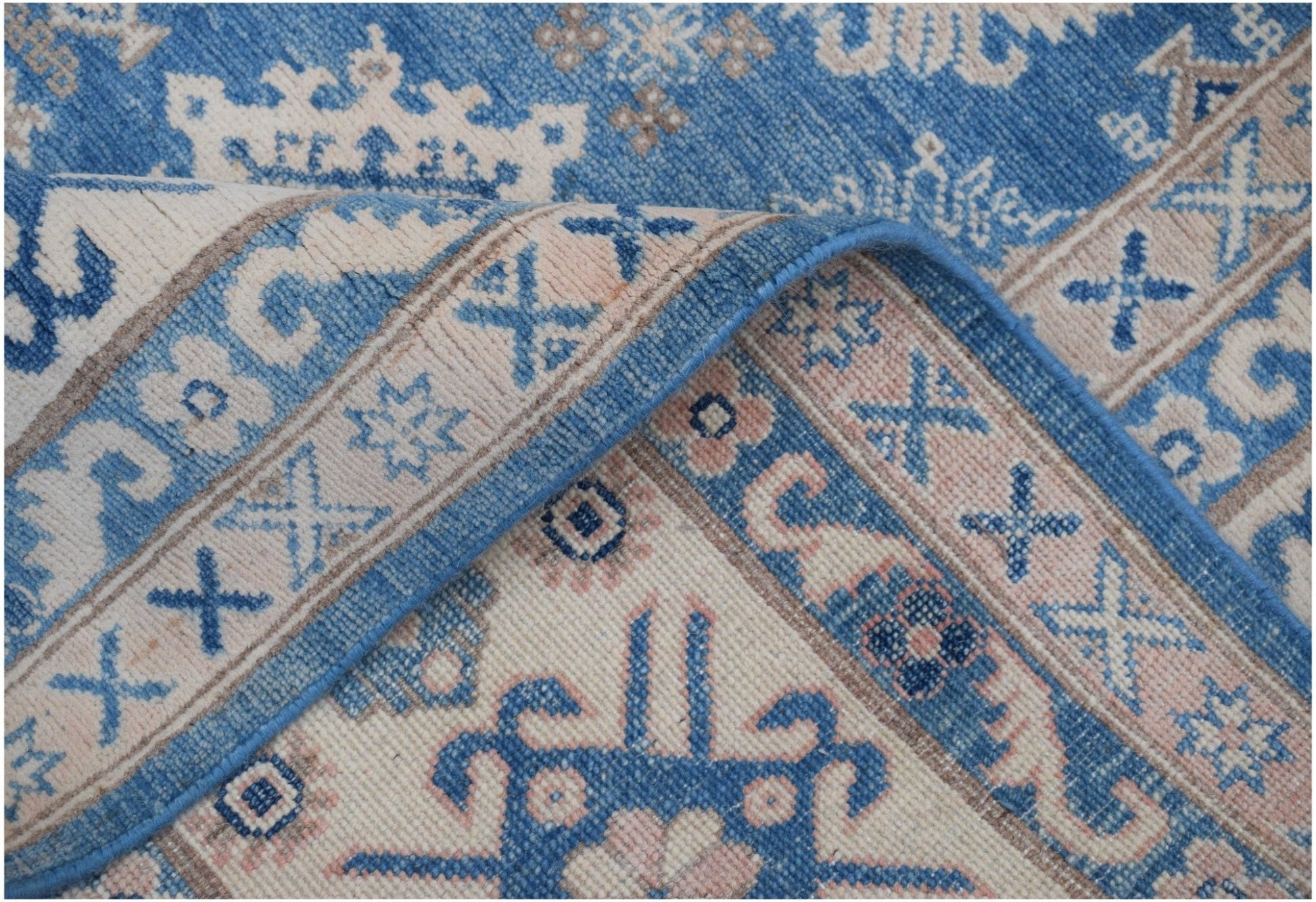 A handmade Afghan Kazakh rug featuring a geometric pattern in shades of blue, beige, and grey.