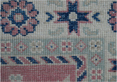 A close-up of an Afghan Kazakh runner featuring traditional geometric motifs in blue and pink wool.