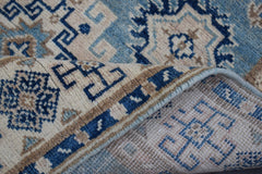 A handmade Afghan Kazakh runner rug featuring a geometric pattern in shades of blue and beige.