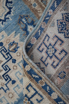 A handmade Afghan Kazakh runner featuring a geometric pattern in shades of blue, beige, and grey.