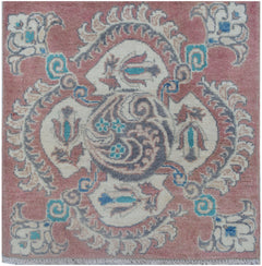 A square Afghan Kazakh rug featuring a central floral medallion in pink, cream, and blue tones.