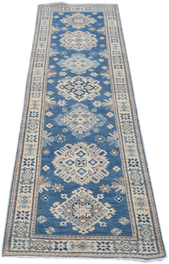 A handmade Afghan Kazakh runner rug featuring a blue field with repeating beige and grey geometric medallions.
