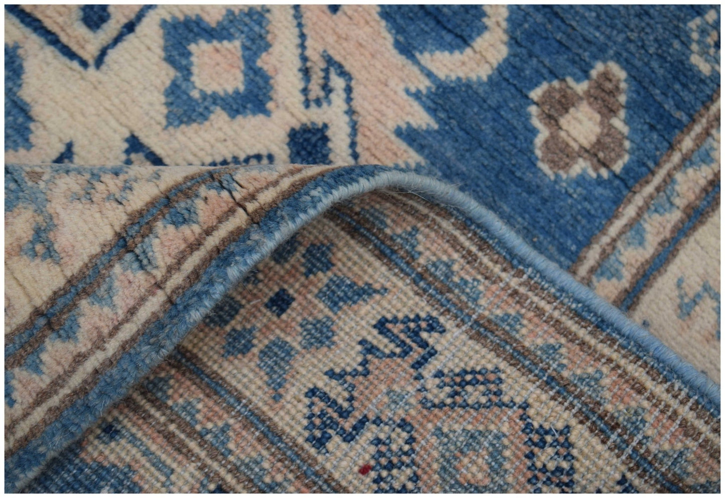 A corner of a handmade Afghan Kazakh runner featuring a blue and beige geometric pattern.
