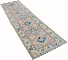 A handmade Afghan Kazakh runner rug featuring a pink field with blue and beige geometric patterns.